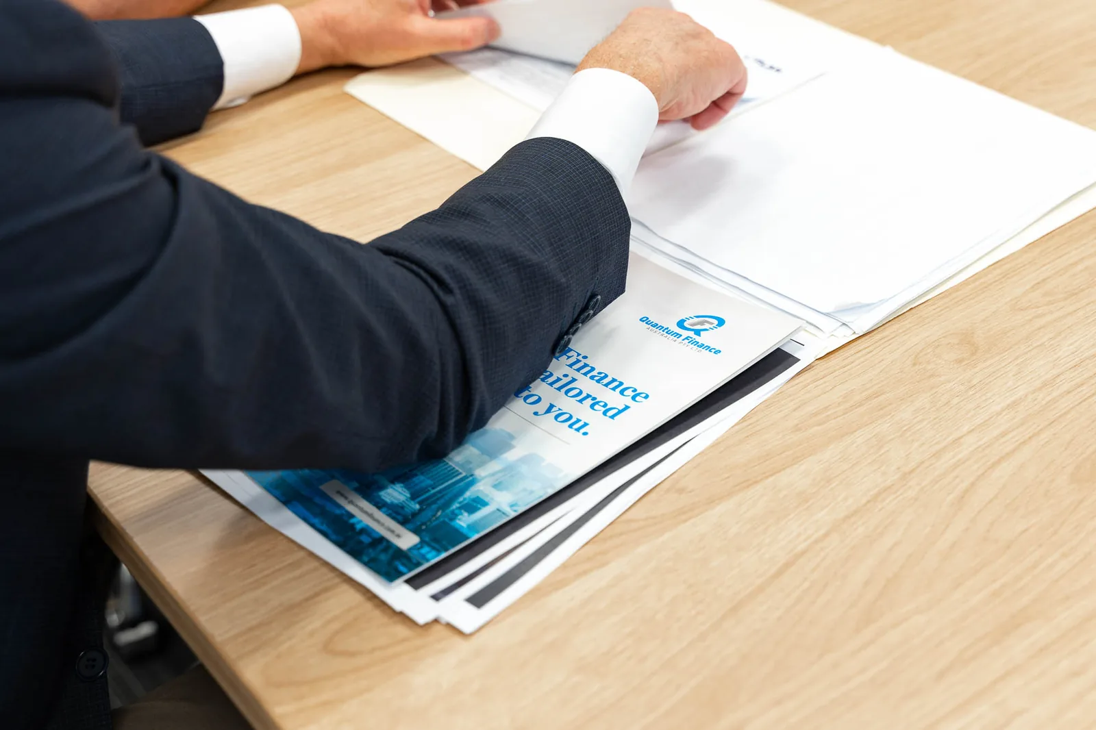 A broker going through Quantum Finance finance brochures at a meeting table