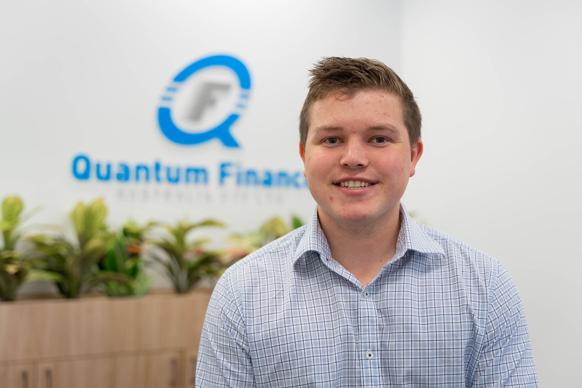 Brodie Kiernan standing in front of Quantum Finance logo.