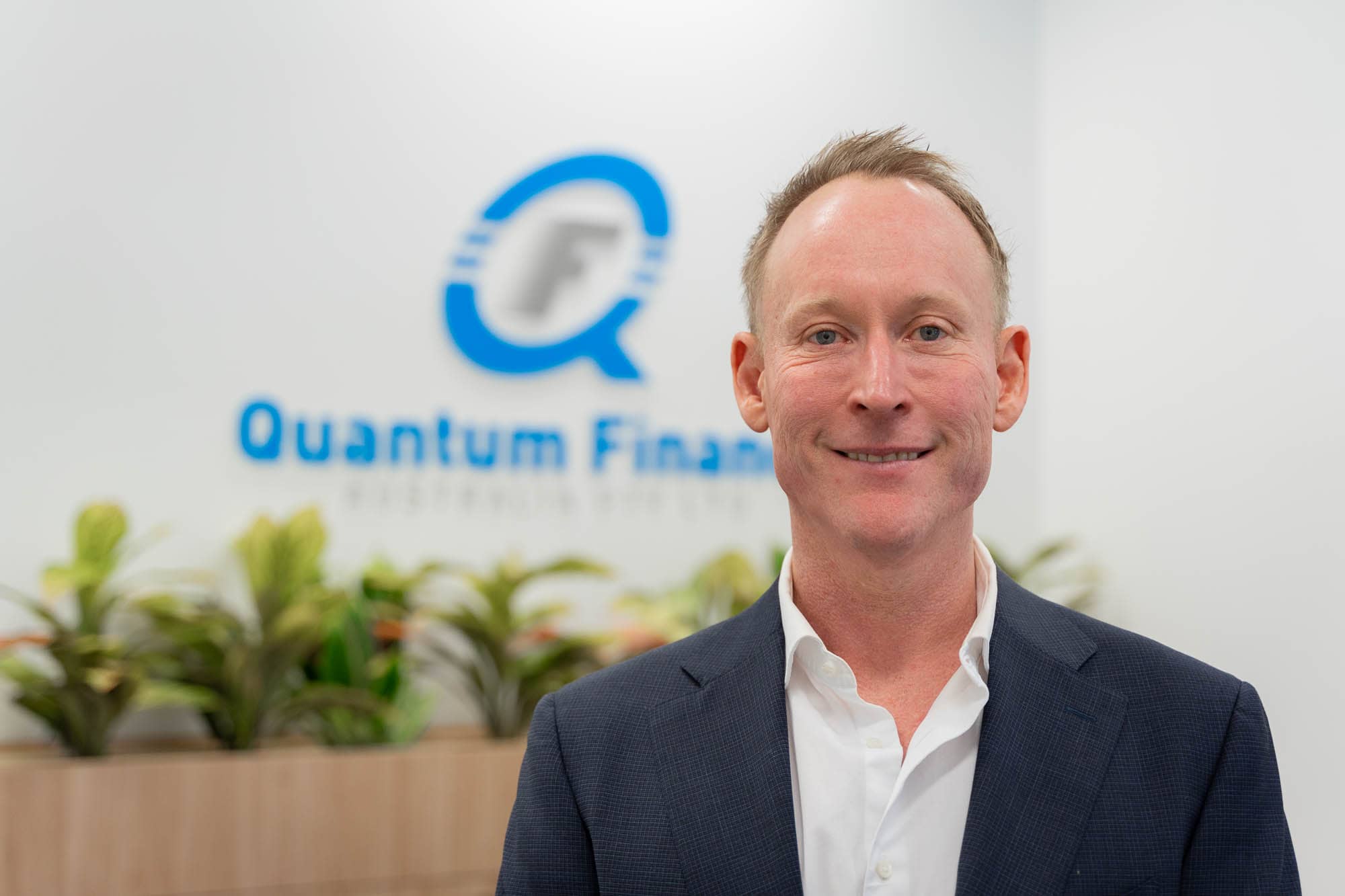 Gavin Harrigan standing in front of Quantum Finance logo.