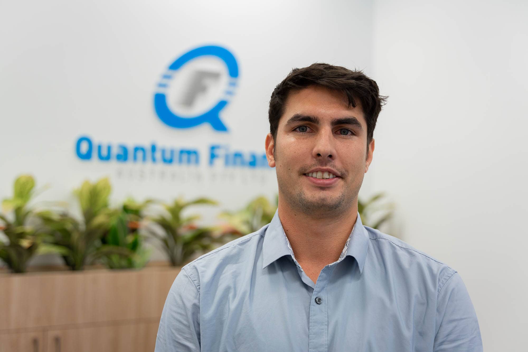 Max Burke standing in front of Quantum Finance logo.